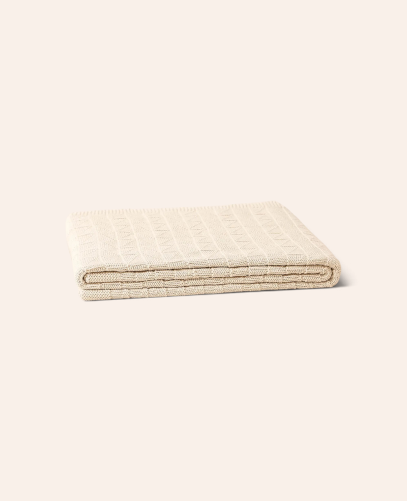 Esmée weiche, beige Strickdecke aus Baumwolle mit modernem Dreiecks-Webmuster, gefaltet auf hellem Hintergrund.