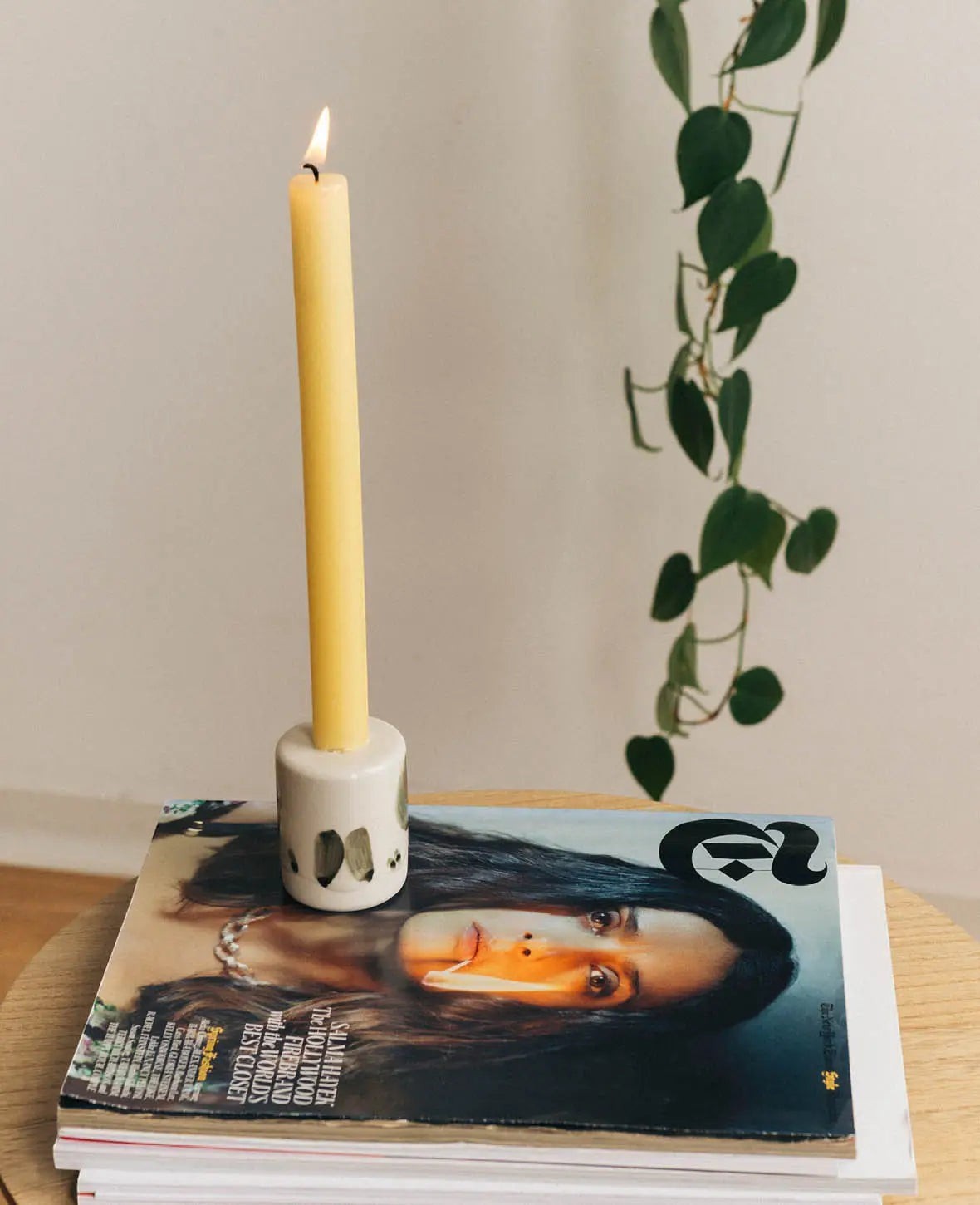 Esmée Keramik Kerzenständer in Weiss mit schwarzen Pinselstrichen, präsentiert mit einer gelben Stabkerze auf Magazinen