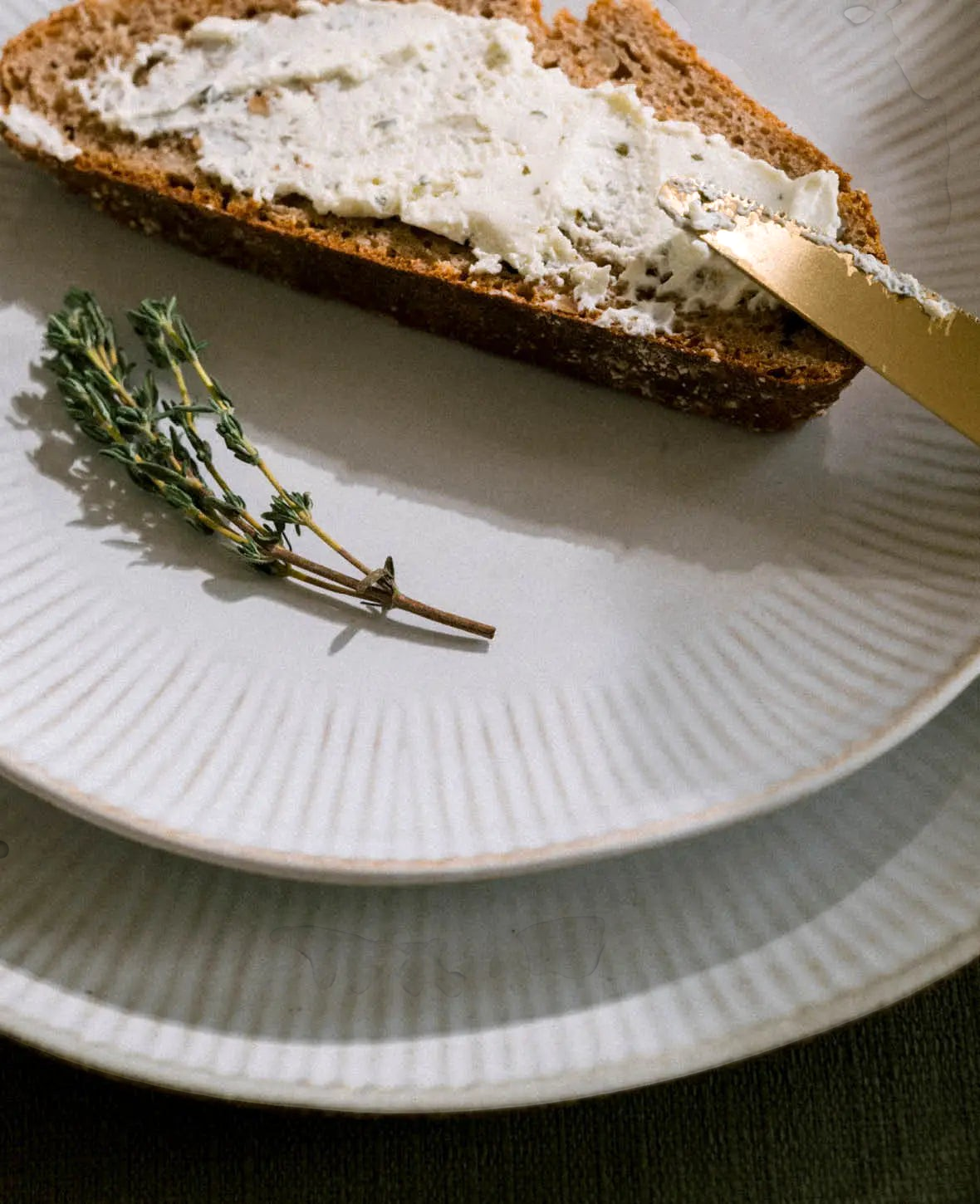 Esmée Nusa Essteller aus Steingut in Off White mit feinem Rillenmuster, serviert mit einer Scheibe Brot und Thymian.