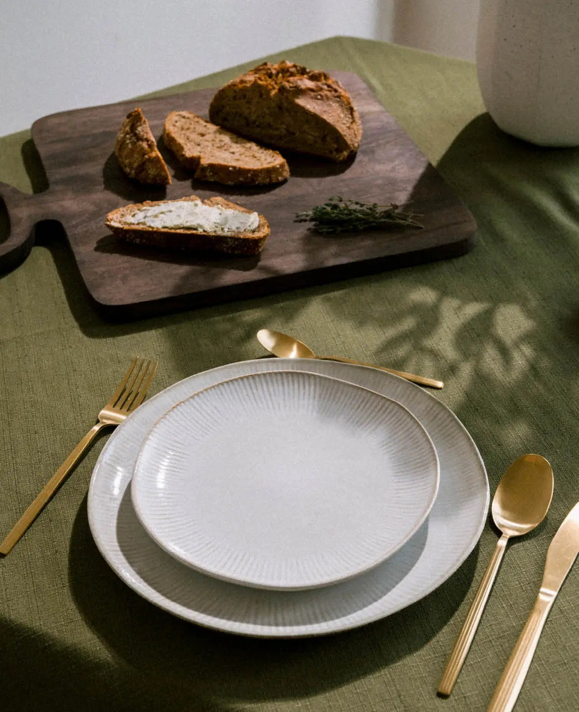 Esmée Schneidebrett aus dunkelbraunem Mangoholz mit Brot auf einem grünen Tisch gedeckt