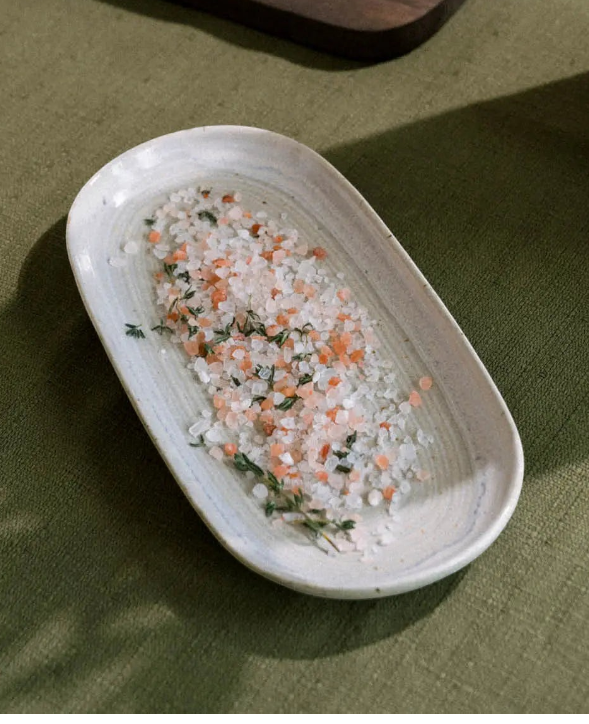 Esmée ovaler Porzellanteller in Off-White mit Himalaya-Salz und Kräutern auf einer grünen Tischdecke