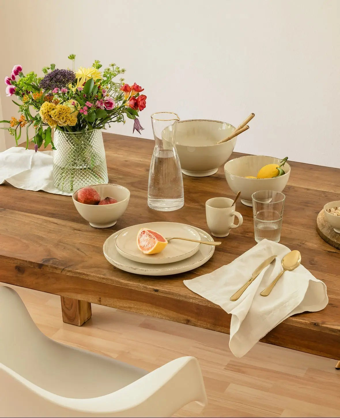 Esmée Keramikschale in Beige auf einem gedeckten Holztisch mit Blumenstrauß und Geschirr