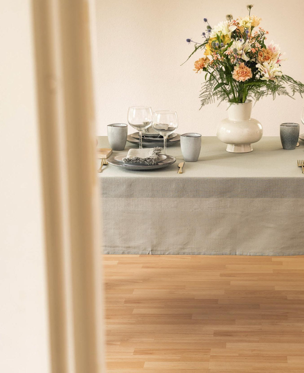 Esmée Villia Tischdecke in Hellgrün auf einem gedeckten Esstisch mit Blumenstrauß und Geschirr